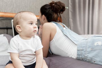 A young mother with a small child works from home, lying on the bed. Quarantine during the coronavirus pandemic.