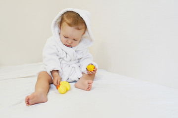 Cute little girl in white towel playing with rubber duck after having bath.