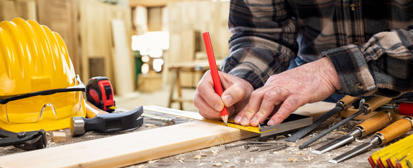 Close-up. Carpenter with pencil and carpenter's square draw the cutting line on a wooden board....