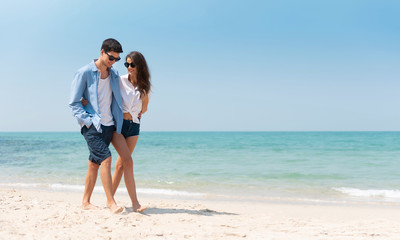 Portrait of Romantic Young couple in casual wear sun glasses walking at the beach with blue sky.