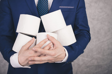 A man in a blue business suit holds 5 rolls of white toilet paper in his hands