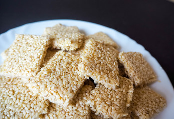 Part of a white steak plate with square shaped cookies of white sesame honey and sugar on a dark background. Gluten free