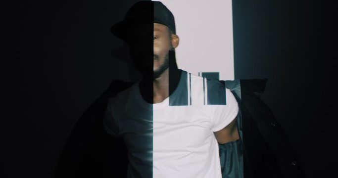 Young sporty African American guy in cap taking off coat with graphic stripes and squares projections. Projected winking pattern and figures on male rapper. Art digital concept.