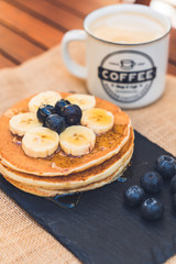 Delicious pancakes with blueberry, bananas and maple syrup on black dish