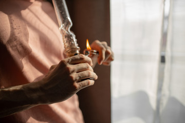 cropped photo of young man heating bong with a lighter. legalization of marijuana, cannabis, hemp...