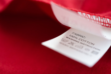 Fototapeta premium White laundry care washing instructions clothes label on red cotton shirt