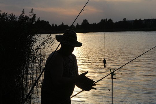 Photo by A fisherman with a hat silhouette by the river against the sunset 