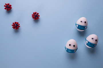 Eggs wearing medical mask for stop coronavirus and models of covid-19 virus on blue background. Epidemic coronavirus COVID-19 concept. Place fo text