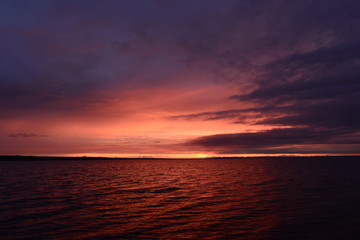 Naklejka na ściany i meble Sun flare in the cloudy sky at sunset on the horizon over water lake