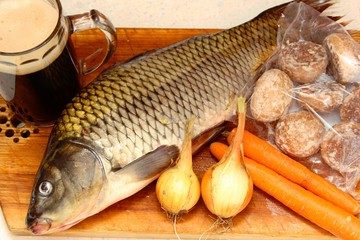 Fresh carp with glas of beer, onion, carrot and cookies on a wooden board, Old Czech fish recipe