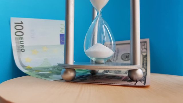 Hourglass on Euro and dollar BANKNOTES on a blue background. Concept-business time money, education, time is running out, time management, time resource, fulltime, deadline