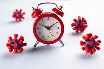 Coronavirus pandemic. Time to stay home .Red alarm clock and and models of covid-19 virus on blue...