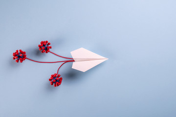 Concept of fly danger. Paper plane and models of covid-19 virus on blue background