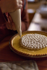 hands of a man using a piping/icing bag to frost a lemon pie