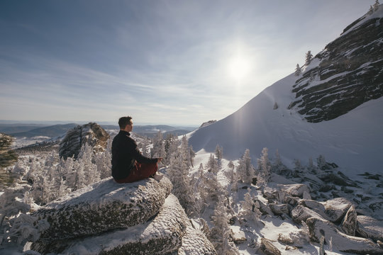 Hiker seating on top of mountain cliff and enjoying the view of valley and winter mountain landscape