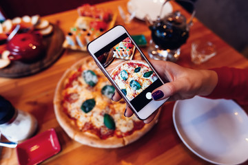 Girl makes a photo of a pizza on a smartphone. Photo of a pizza