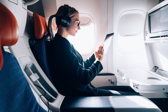 Travel tourism with modern technology and air flights concept, Caucasian woman sitting in plane with modern digital gadget and searching favourite music playlist in application for listening