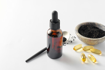 Glass bottle and pills of black cumin seeds essential oil. Nigella Sativa in spoon and bowl on white background