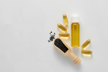 Bottle and pills of black cumin seeds essential oil. Nigella Sativa in wooden spoon on white background