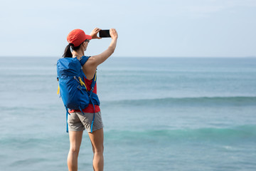 Woman hiker in seaside using smartphone taking pictures