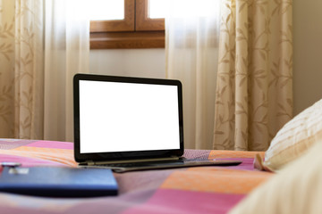 Photography of a laptop in bed while remote working from home and a bright window in the background. Template advertising.