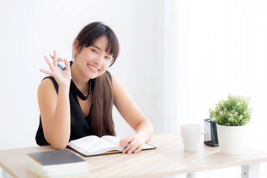 Beautiful portrait young asian woman smiling sitting study and learning writing notebook and diary in the living room at home, girl homework, business woman working on table, education concept.