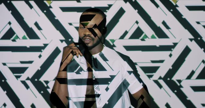 African American young handsome guy moving and dancing on white wall background with graphics and triangles projections. Projected pattern and figures on male dancer. Art digital concept.