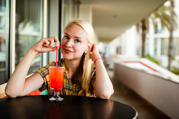 Portrait of a young woman drinking a cocktail and smiling, looking at the camera.