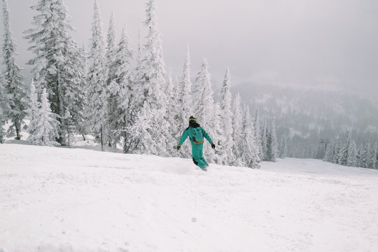 Freerider snowboarder wearing snowboard jumpsuit riding in winter snow-covered forest