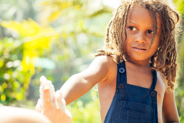 Mowgli indian boy with dreadlocks hair hiding holding mosquito spray in tropics green forest background