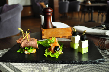 Assorted canapes, roast beef with salmon olives with cucumber and feta cheese on a board