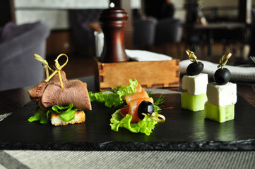 Assorted canapes, roast beef with salmon olives with cucumber and feta cheese on a board