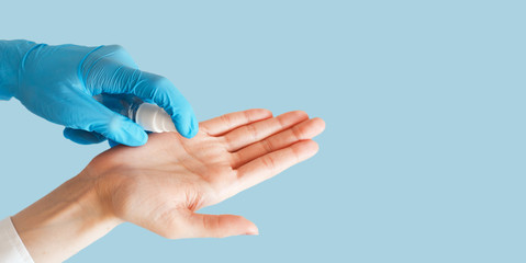 Hand in medical gloves applying sanitizer gel on blue background