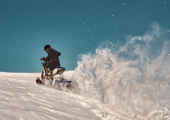 Fototapeta na wymiar Snowbike rider in mountain valley. Modify dirt bike with snow splashes and trail. Snowmobile sport riding, winter sunny day