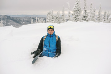 Fototapeta na wymiar Snowboarder free rider man walking on snowy slop, snow covered trees on background, bad weather, siberian winter snow powder day in ski resort