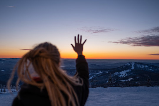 Female hand out of focus on mountains landscape and sunset sky background