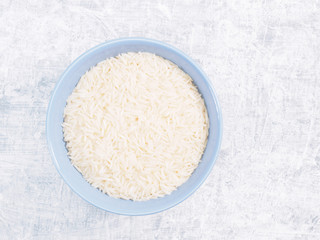 Indian long grain Basmati rice in blue ceramic bowl on white concrete background
