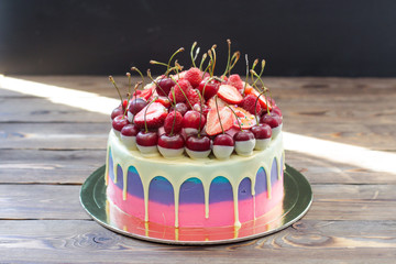 Pink and blue colored cake with melted white chocolate with fresh cherries, raspberries and...