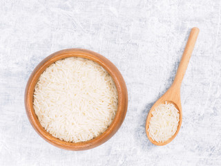 Indian long grain Basmati rice in brown wooden bowl and spoon on white concrete background