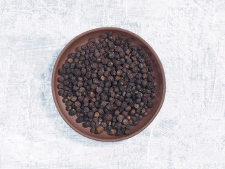 Spice black pepper in clay plate on white concrete background