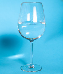 The glass is half filled with water. A glass of water is standing on a gulb background. Healthy food concept
