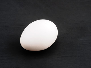 One white chicken egg on a black wooden background. Healthy eating concept
