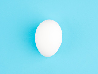 Fototapeta na wymiar One white chicken egg on a blue background. Healthy eating concept