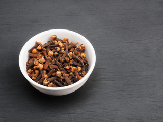 Spice cloves in white ceramic bowl on black wooden background. Healthy eating and organic food concept