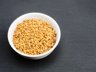 Spice fenugreek in white ceramic bowl on black wooden background. Healthy eating and organic food concept