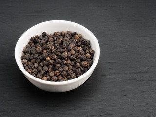 Spice black pepper in white ceramic bowl on black wooden background. Healthy eating and organic food concept