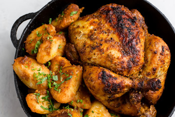 Baked whole chicken with potatoes and herbs in a rustic style. Top view, side view on a light background. Close-up and medium plan. Space for text.