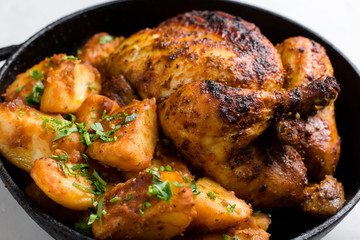 Baked whole chicken with potatoes and herbs in a rustic style. Top view, side view on a light background. Close-up and medium plan. Space for text.
