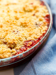 Traditional British Red berry crumble in glass baking dish with cloth on white background. Close up. Delicious dessert in rustic style, selective focus
