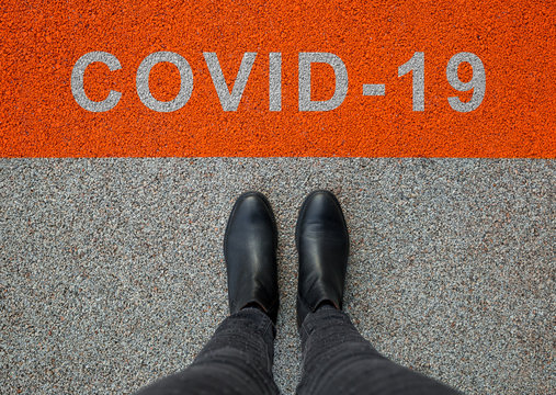 Black shoes standing on the asphalt concrete floor with orange line. Feet shoes walking in outdoor. Coronavirus in the world. COVID-19 alert banner.